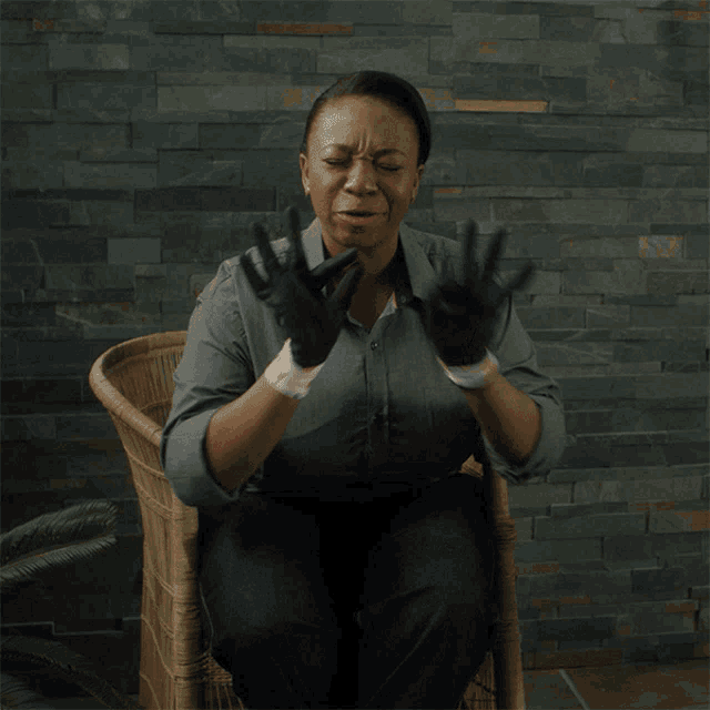 a woman wearing black gloves is sitting in a wicker chair