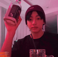 a young man wearing a purple hat is holding a bottle of vodka .