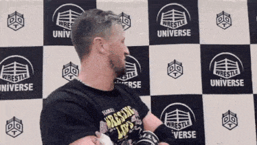 a man in a black shirt is standing in front of a checkered wall with logos on it .