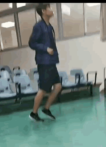 a man in a blue jacket and black shorts is running on a green floor in a waiting room .