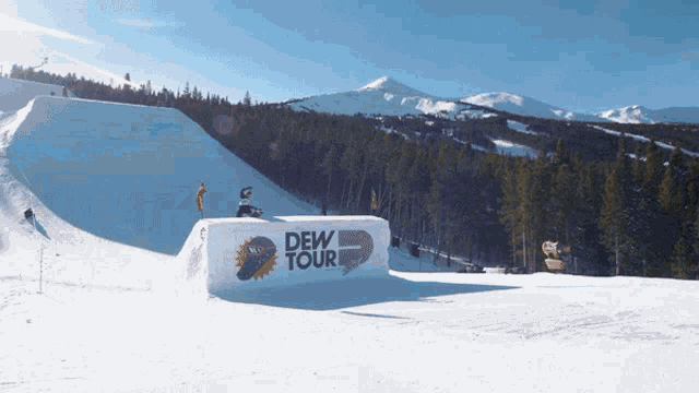 a snowboarder is doing a trick in front of a sign that says " dew tour "