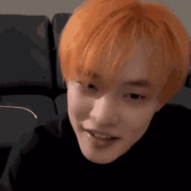 a man with orange hair is sitting on a couch and smiling .
