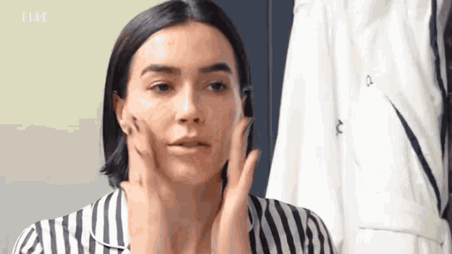 a woman in a striped shirt is looking at her face in a mirror .
