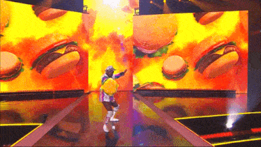 a man is dancing on a stage in front of a large screen of hamburgers .