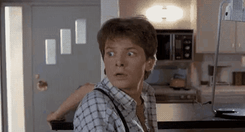 a man in a plaid shirt is standing in a kitchen looking surprised .