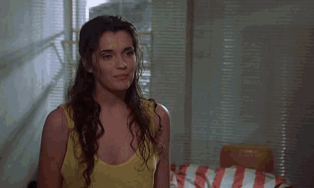 a woman in a yellow tank top stands in front of a bed