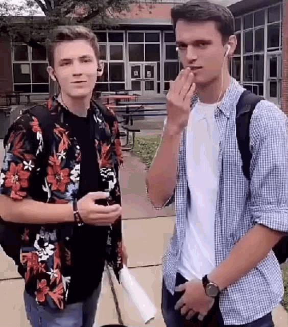 two young men are standing next to each other on a sidewalk in front of a building .