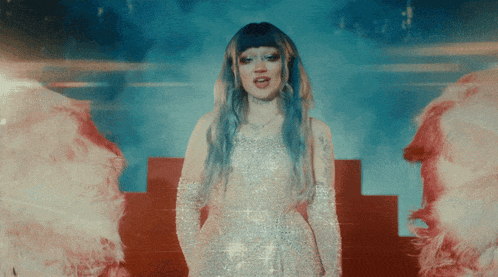 a woman with blue hair is standing in front of a fire