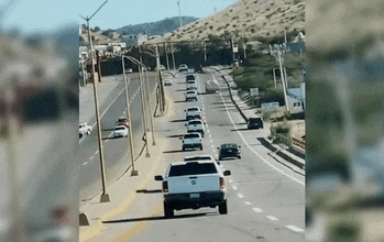 a row of cars are driving down a highway next to a mountain .