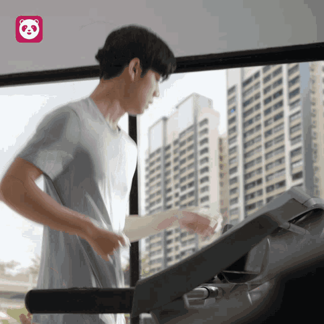 a man is running on a treadmill in front of a window with a panda icon in the corner