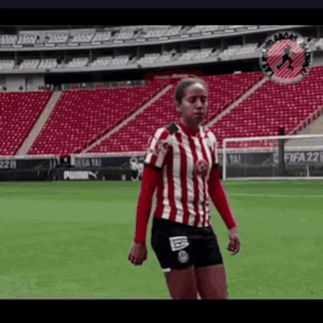 a woman in a red and white striped shirt is standing on a soccer field in front of an empty stadium .