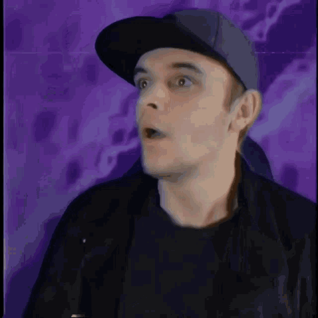 a man wearing a baseball cap and a black jacket is making a surprised face