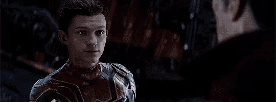 a young man in a spiderman suit is standing next to a man in a black suit in a dark room .