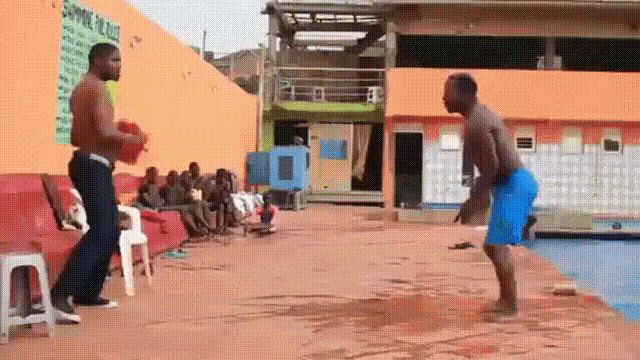 two men are standing next to each other on a concrete surface in front of a pool .