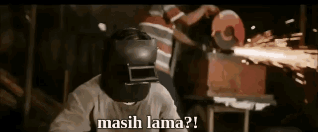 a man wearing a welding helmet is cutting something with a grinder .