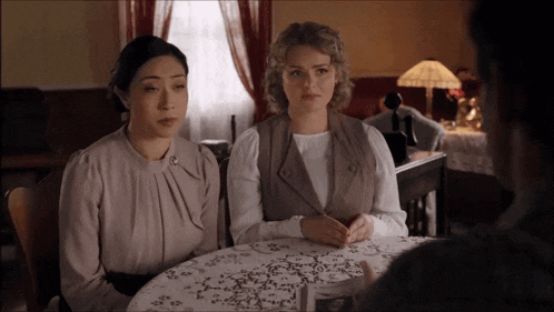 two women are sitting at a table with a man talking to them