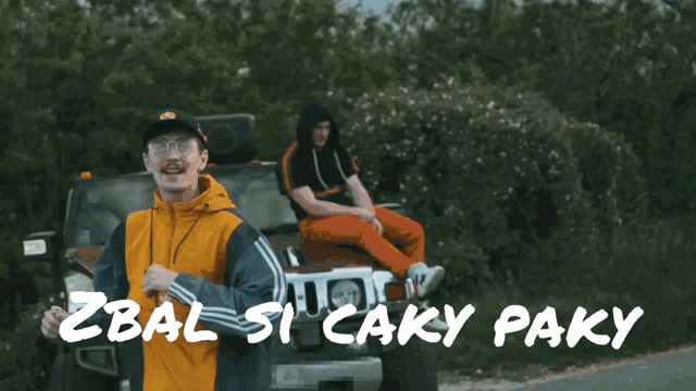 a man in an orange jacket is standing in front of a car with the words zbal spcaky paky written on the bottom