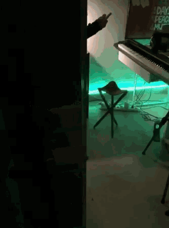 a person is standing in front of a piano in a dark room with a green light behind them