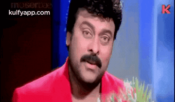 a man with a mustache is wearing a red jacket and a red shirt .
