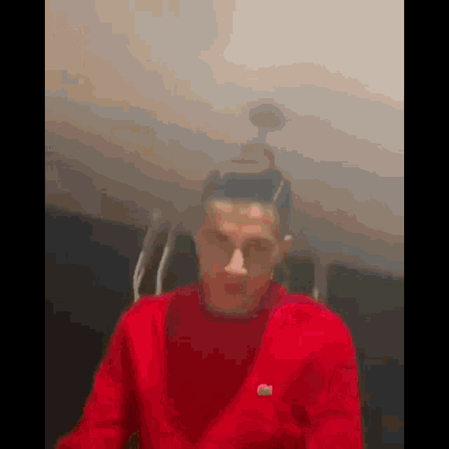 a man in a red sweater is smoking a cigarette in a room with smoke coming out of his head .
