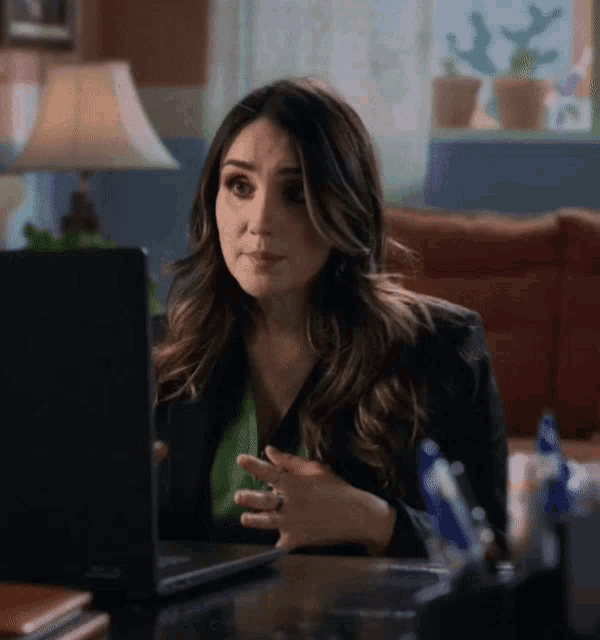 a woman is sitting at a desk looking at a laptop computer
