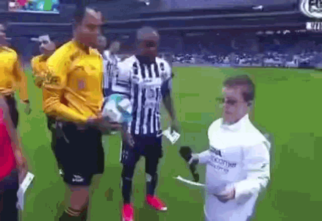 a man in a white shirt is holding a microphone and talking to a soccer player on a field .