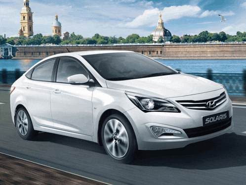 a white hyundai solaris is driving down a road near a body of water