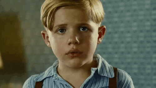 a young boy wearing suspenders and a blue shirt looks at the camera