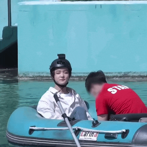 a man wearing a helmet is sitting in a raft with a man in a red shirt standing behind him .