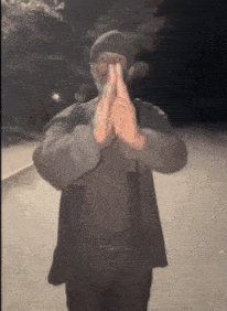 a man wearing a beanie and a jacket holds his hands together in a prayer