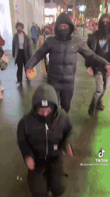 a group of people are walking down a street wearing masks and hoodies .