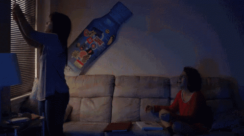 two women are sitting on a couch in front of a large coca cola bottle