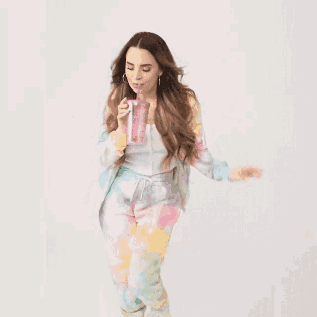 a woman in a tie dye outfit holding a pink cup