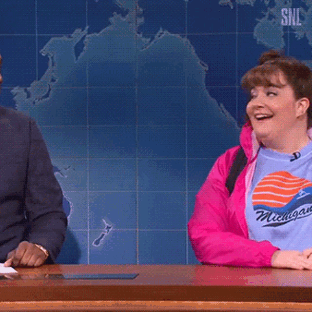 a woman wearing a shirt that says michigan sits at a desk