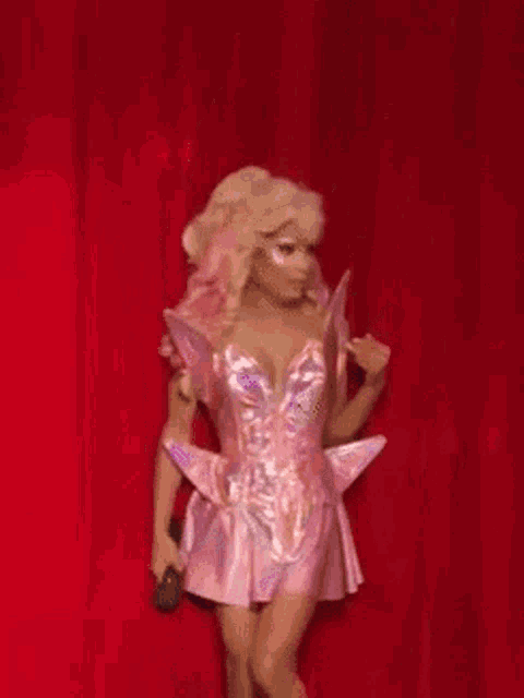 a woman in a pink dress is holding a microphone in front of a red curtain