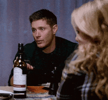 a man is sitting at a table with a bottle of wine on it .