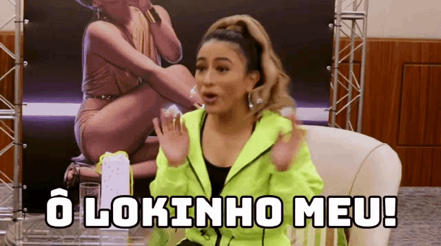 a woman in a neon green jacket is sitting in front of a poster that says o lokinho meu