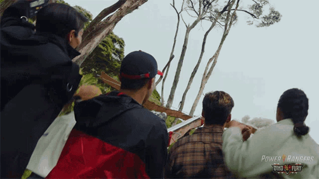 a group of people are looking up at a tree with a power rangers logo in the corner