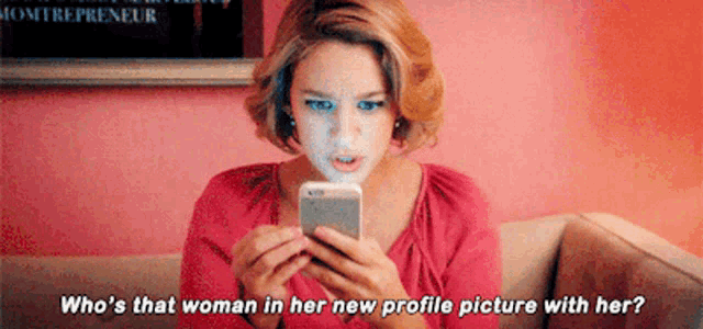 a woman is sitting on a couch looking at her phone and asking who 's that woman in her new profile picture with her ?