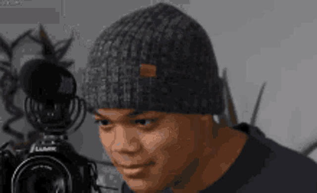 a man wearing a gray beanie is looking at a lumix camera