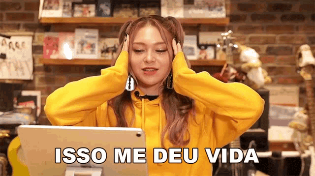 a woman in a yellow hoodie is looking at a tablet with the words isso me deu vida written below her