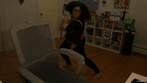a woman is standing in front of a chair with a twitch logo on the shelf behind her