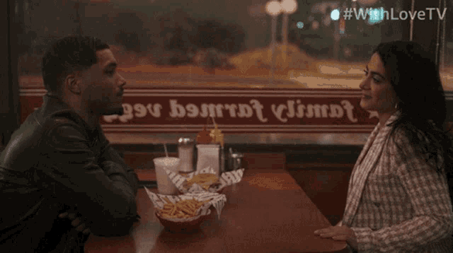 a man and a woman are sitting at a table in front of a window that says ' with love tv '