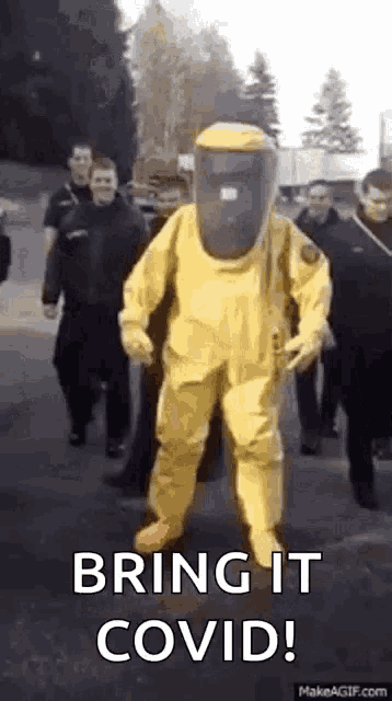 a man in a yellow hazmat suit is walking down a street with a group of people .