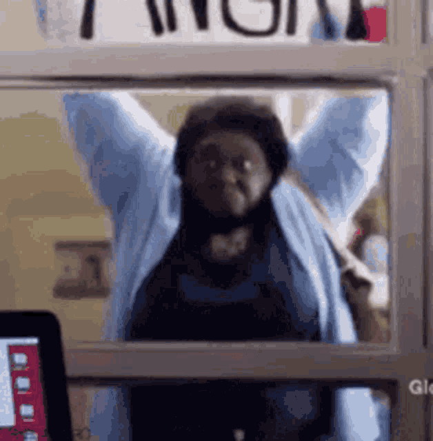 a woman is standing in front of a window with her arms up .