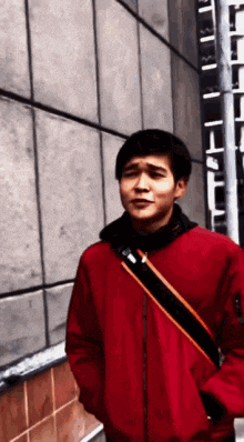 a young man in a red jacket is standing in front of a wall .
