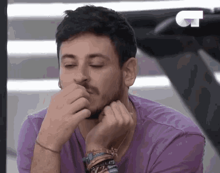 a man in a purple shirt is covering his face with his hands