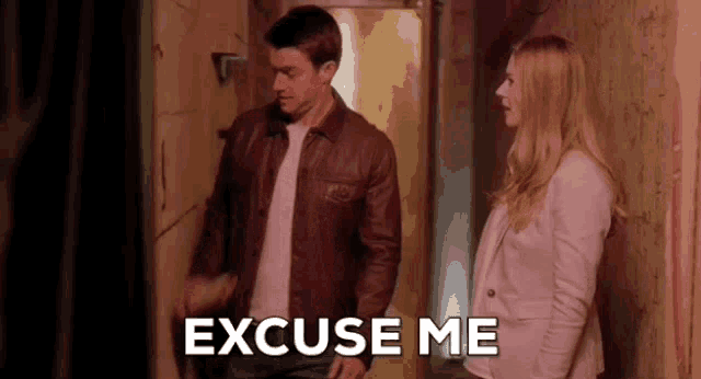 a man and a woman are standing next to each other in a hallway and the woman is saying excuse me .