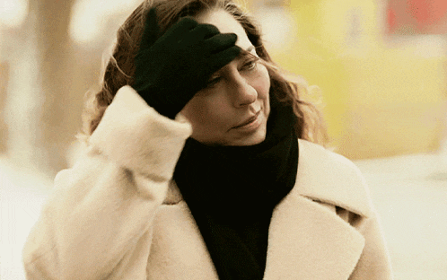a woman wearing a black scarf and a white coat holds her hand to her head