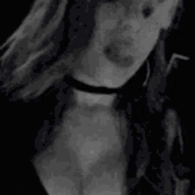 a woman wearing a choker and earrings is smoking a cigarette in a black and white photo .